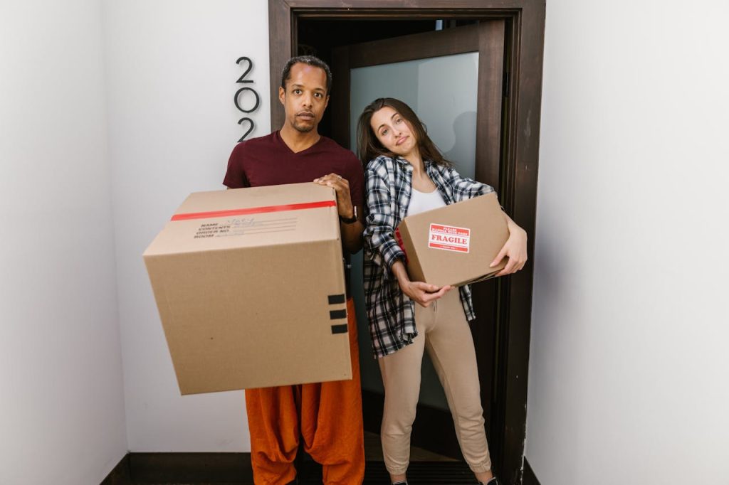 A couple carrying moving boxes indoors, settling into their new apartment.