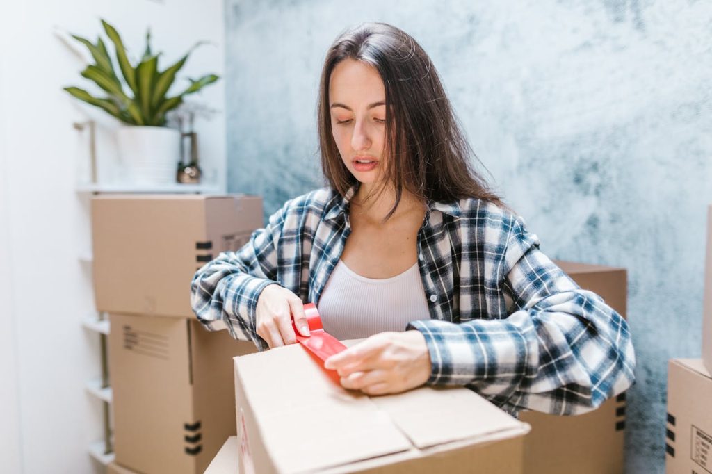 Woman sealing boxes with tape for relocation in a cozy indoor setting.