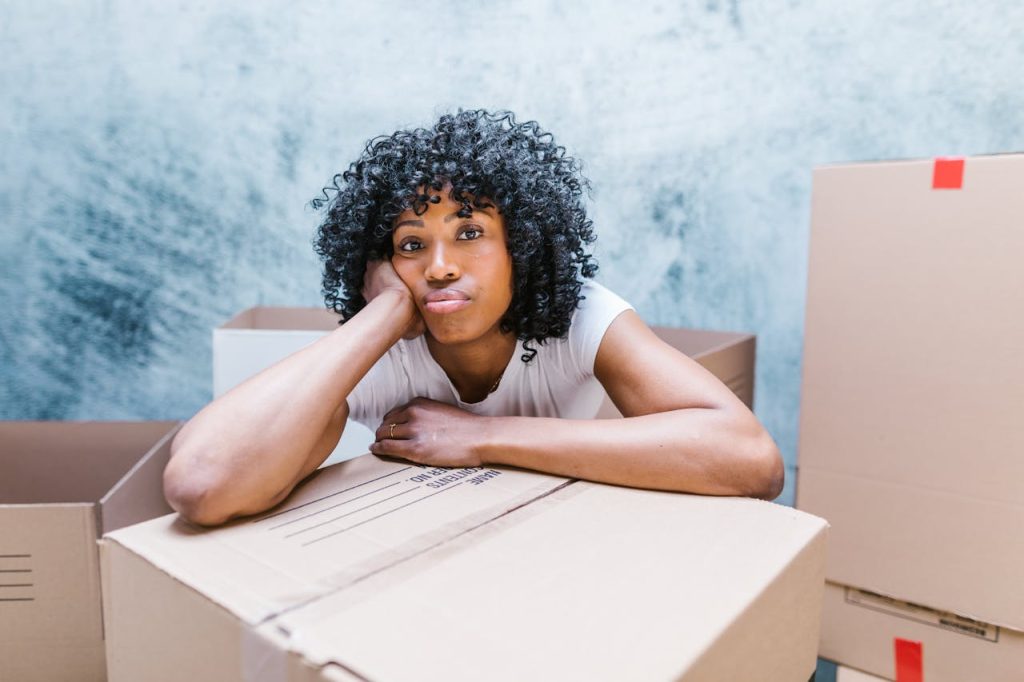 Tired woman leaning on a moving box while packing and relocating to a new home.
